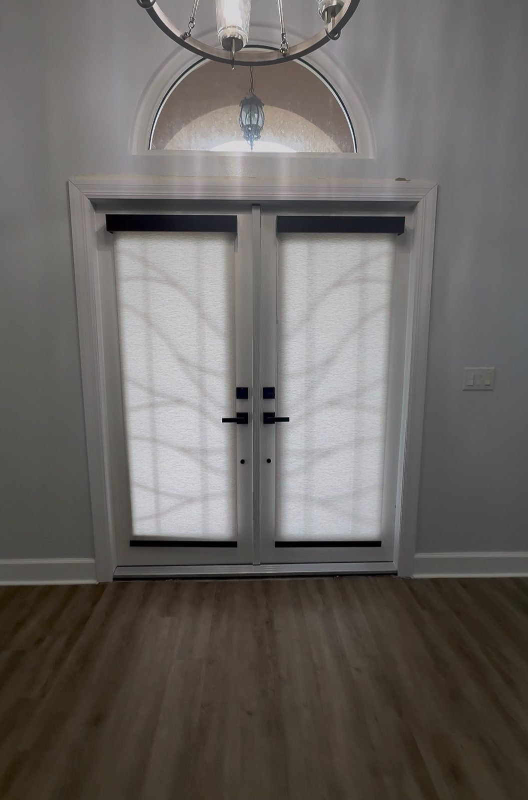 White light-filtering roller shades fitted to a pair of French entry doors under an arched transom