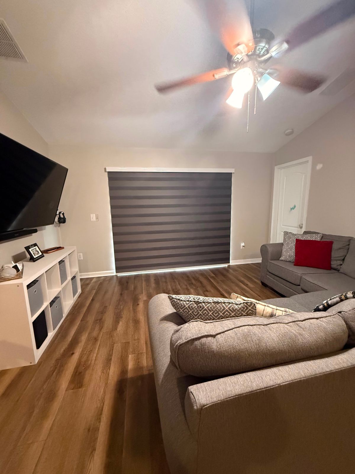 Charcoal zebra shade covering a wide sliding glass door in a family room with wood-look floors